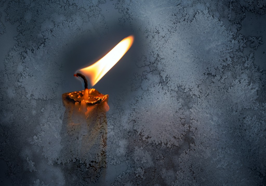 Closeup Photo Of Little Candle Flame Behind Frozen Window Glass